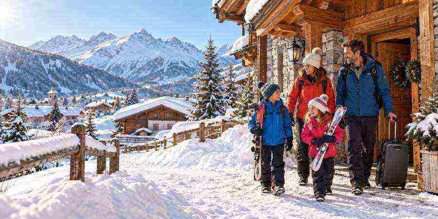 Famille arrivant devant un chalet enneigé pour des vacances au ski avec enfants.